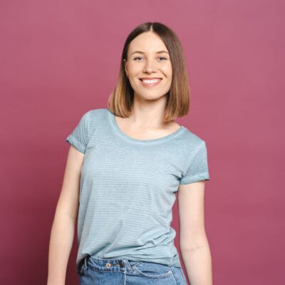 Portrait of smiling woman standing folded hands wearing casual blue tshirt isolated on pink background with copy sace